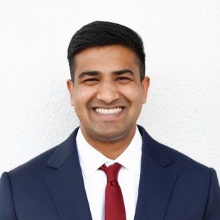 An image of Dr Revanth Chada wearing a navy blue blazer and a red necktie over a white shirt.